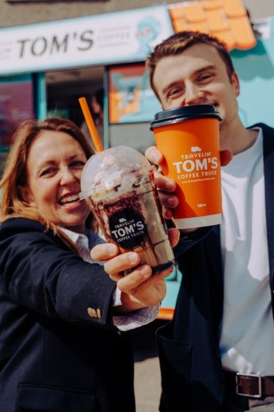 Travelin' Tom's Corporate Events1 Two staff members at a corporate gathering smile and raise their Travelin’ Tom’s cups to the camera