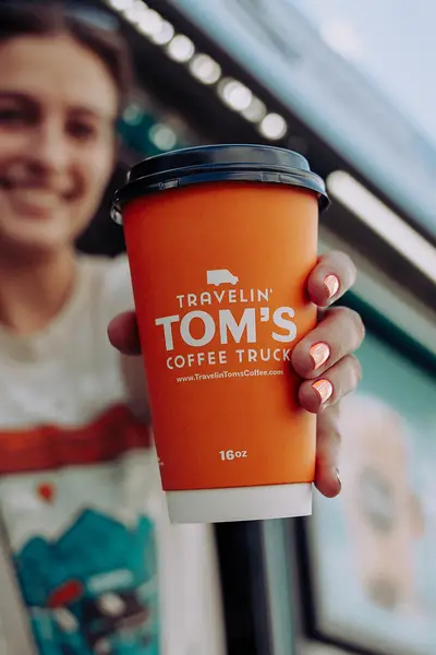 A woman holding a vibrant orange hot coffee cup from Travelin' Tom's Coffee Truck