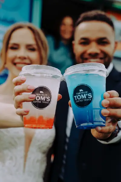 Close-up of Travelin' Tom's strawberry boba and Berry TILT Nitro Energy™ beverages held toward the camera by a bride and groom