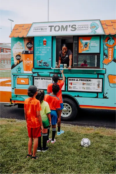 Athletes line up at a Travelin' Tom's Coffee Truck as a franchise owner serves specialty drinks after a sporting event