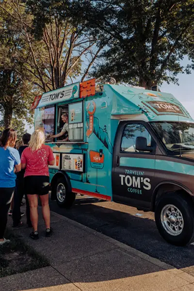 A line of customers gathering around a Travelin' Tom's Coffee Truck as the owner hands out specialty beverages