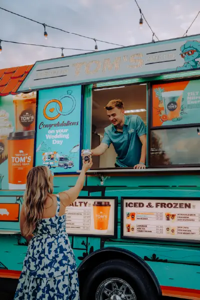 A woman in a dress receives a frozen specialty drink from a Travelin' Tom's Coffee Truck at a wedding