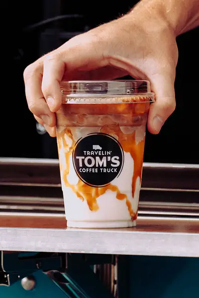 Close-up of a hand holding an iced caramel macchiato with caramel drizzle in a branded cup from a Travelin' Tom's Coffee Truck