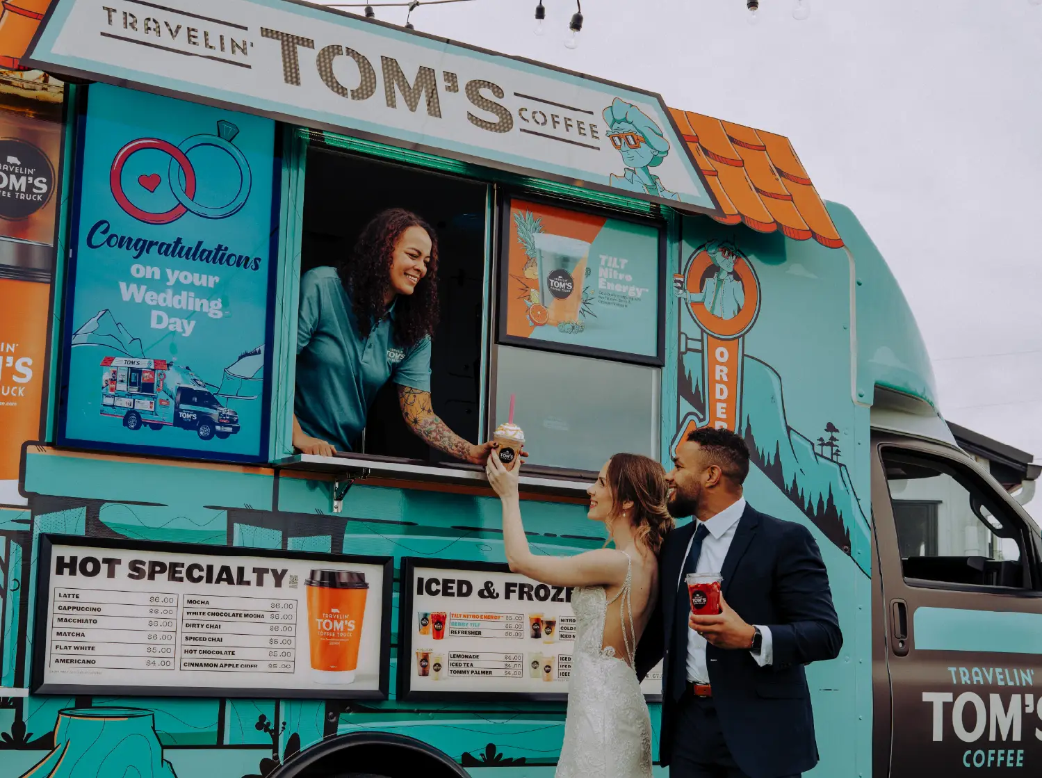 A bride and groom receive a frozen coffee drink from a Travelin' Tom's Coffee Truck displaying a custom wedding message